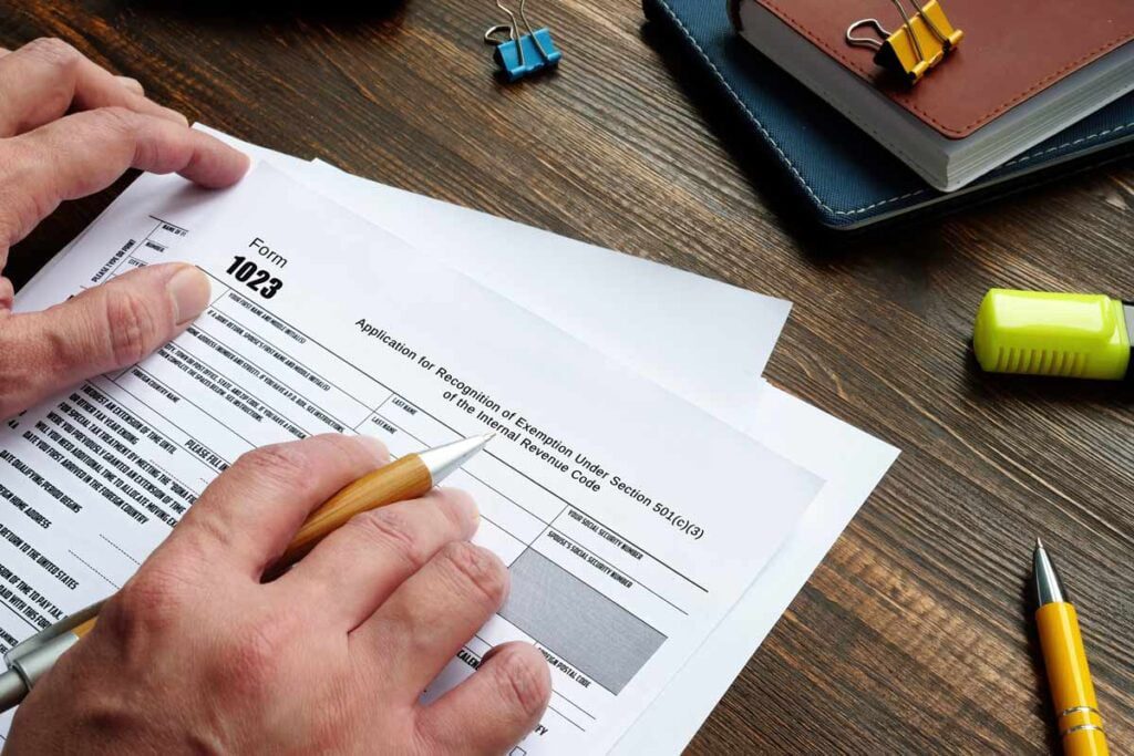 hand filling out a form titled "Application for recognition of exemption under section 501(c)(3) of the internal revenue code"