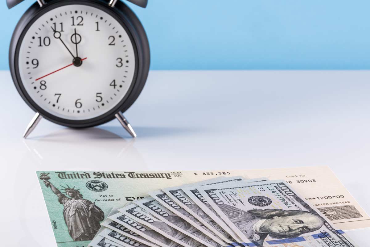 alarm clock beside a stack of money and a treasury check