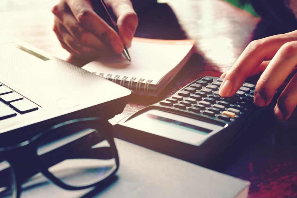 hands writing on notepad and typing on calculator