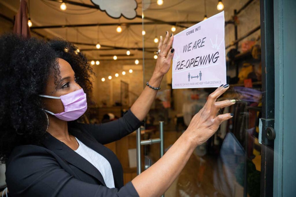 sign saying "we are reopening" is being hung by woman in mask