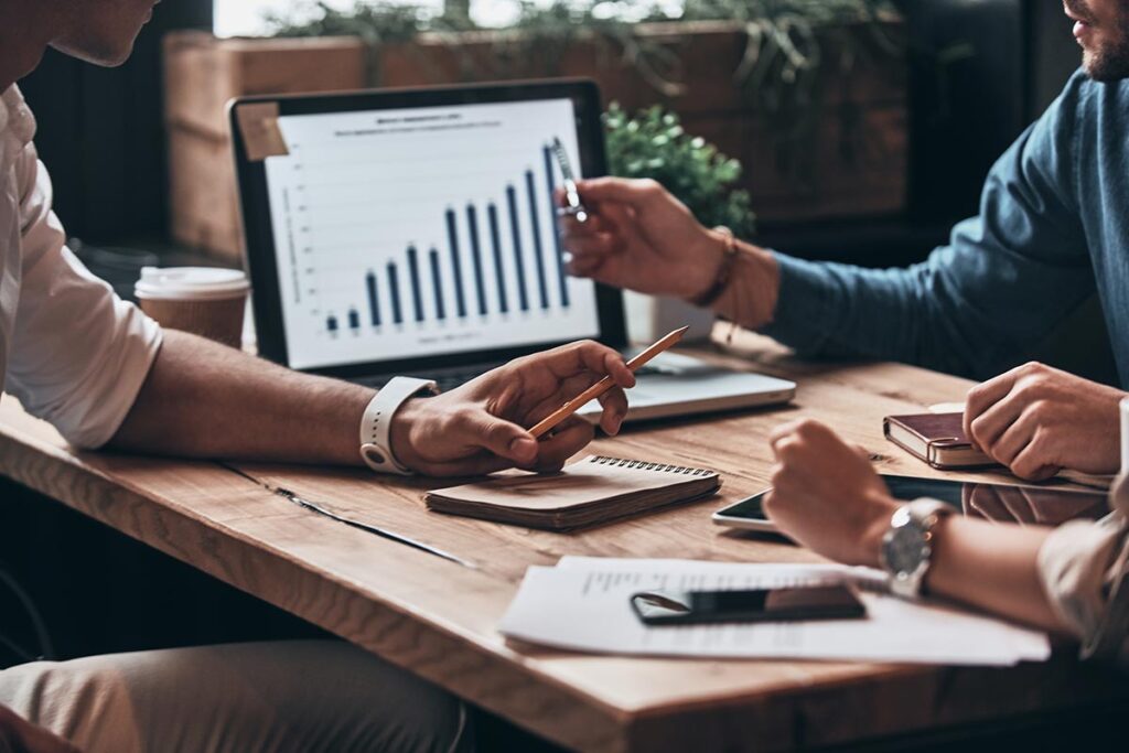 meeting with multiple people siting at a table in front of a laptop screen with a chart on it