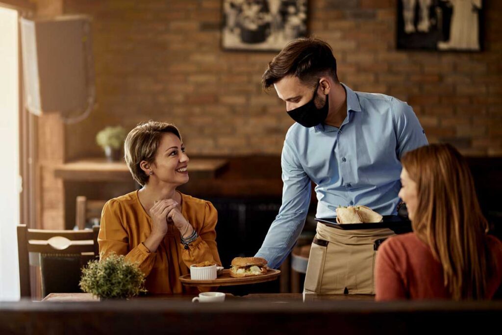 masked waiter serves food to 2 patrons