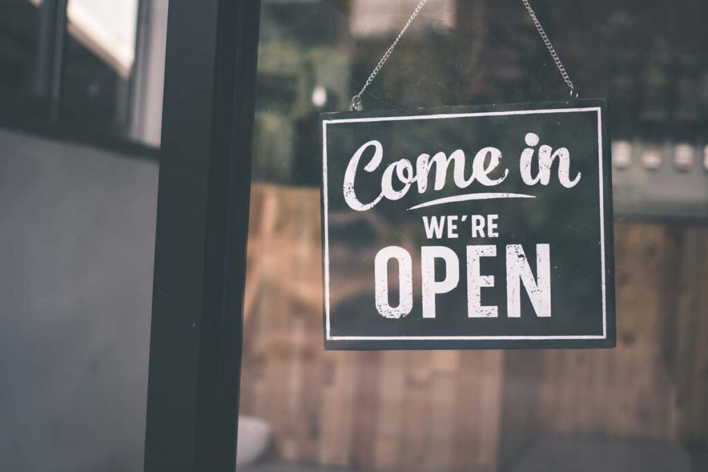 sign in shop window saying "come in, we're open"