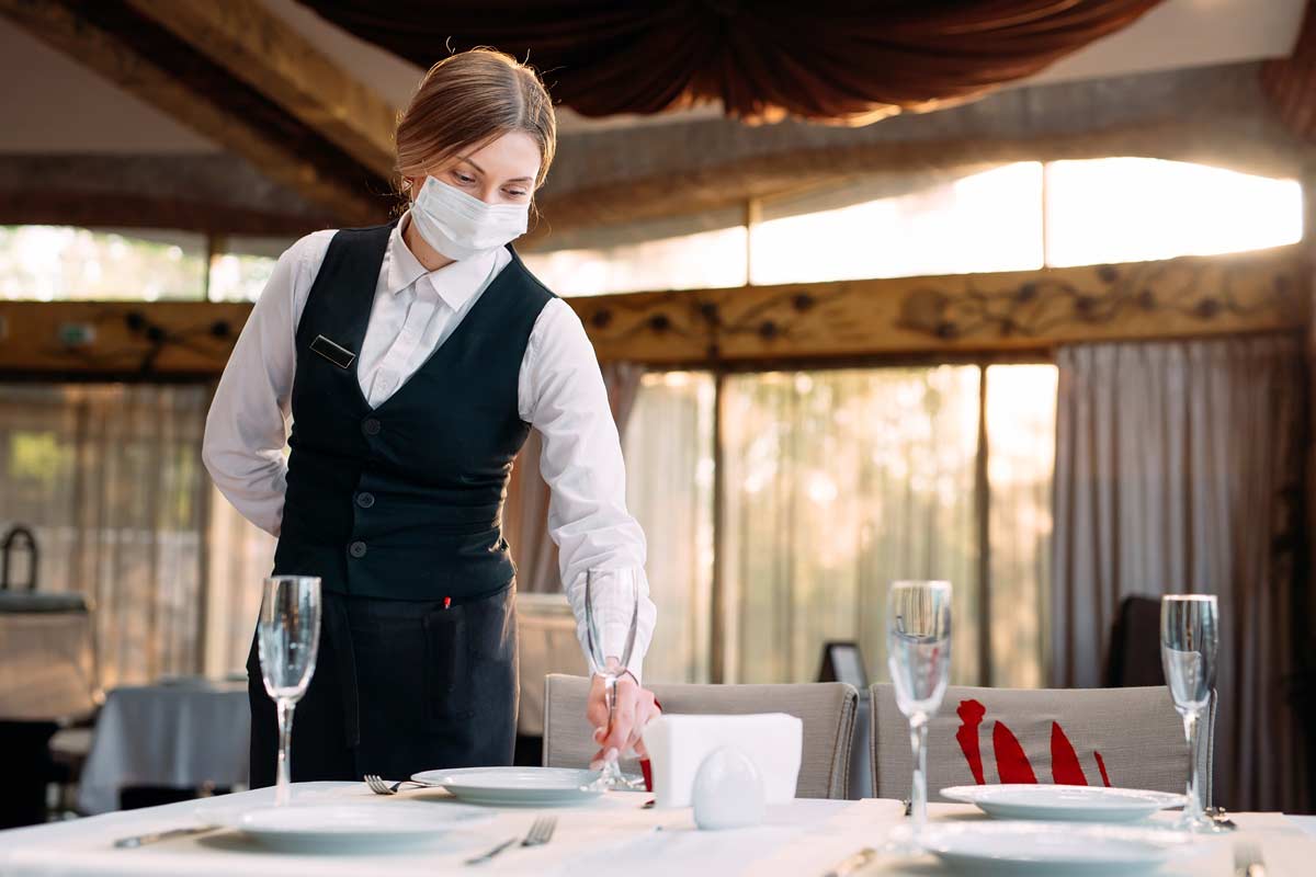 waiter in protective mask sets a table