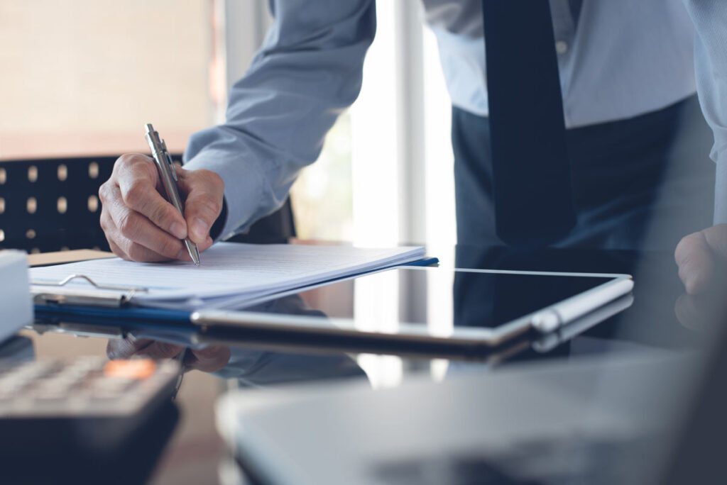 a hand writing on paper next to a tablet