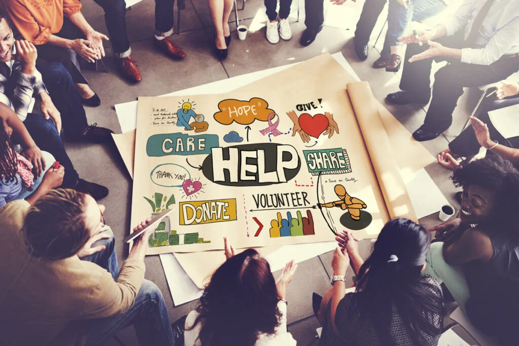 people sitting in a circle around paper that reads "Help, Care, Hope, Give, Share, Donate, and Volunteer"