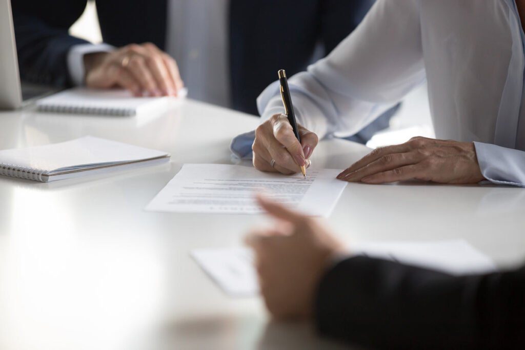 hands writing at a desk with other people around it