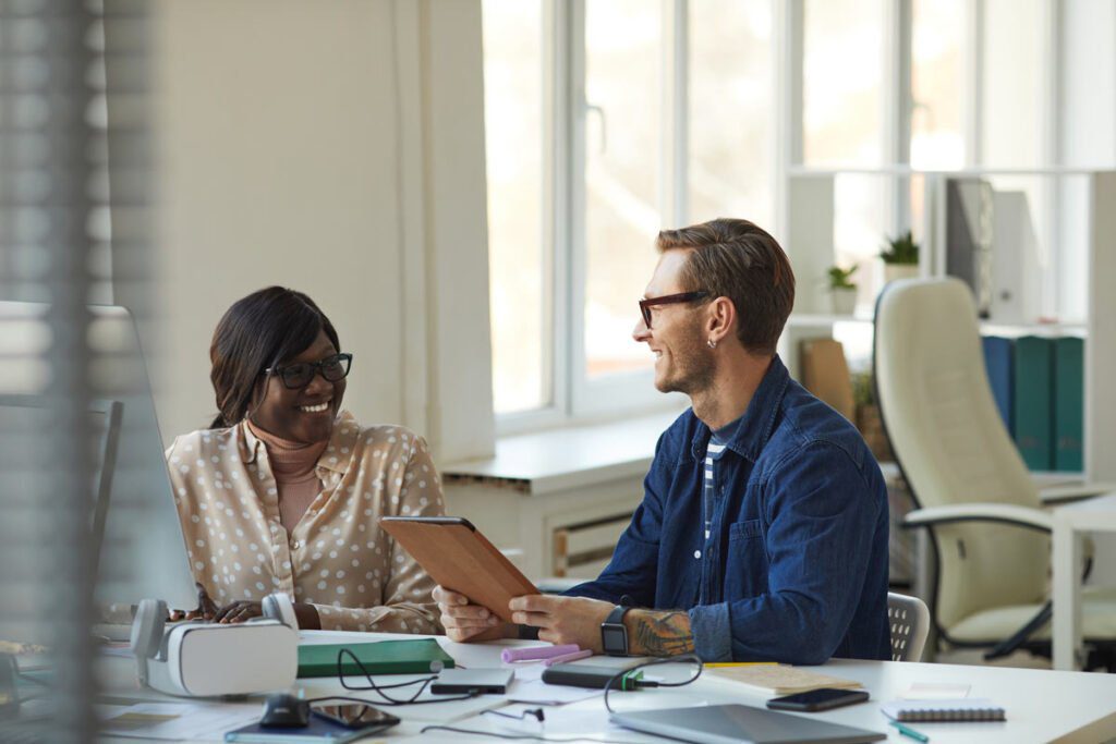 2 colleagues smiling and working at a desk