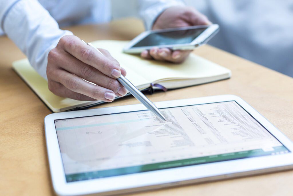 hands with pen pointing at a spreadsheet on a tablet