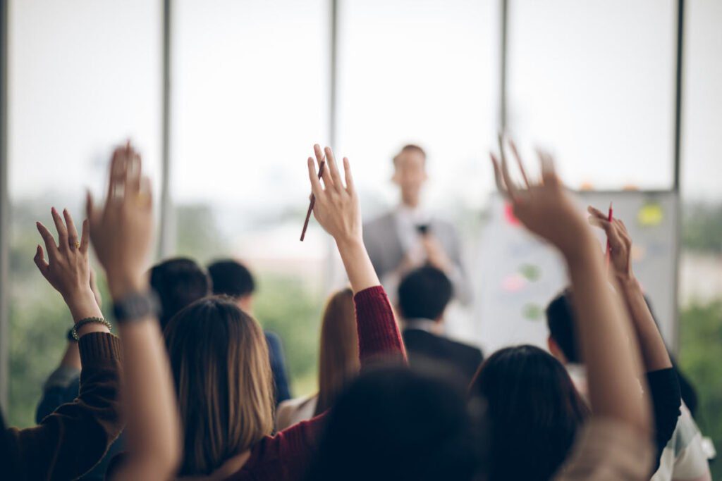 hands raised in a crowd with a speaker blurred in the background