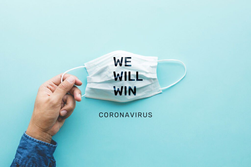 hand holding a mask that says "we will win" on it with the word "coronavirus" printed below