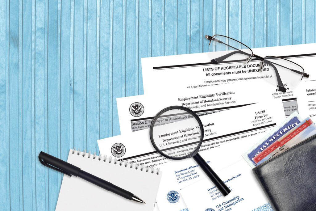 "Employment Eligibility Verification" Documents with magnifying glass, glasses, notepad and a wallet with a social security card sliding out of it