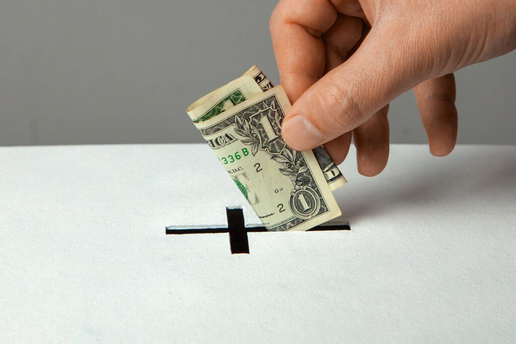 a dollar being placed into a hole shaped like a cross