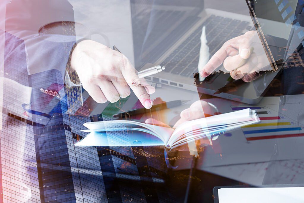 hands pointing at a notebook and computer overlaid over a city