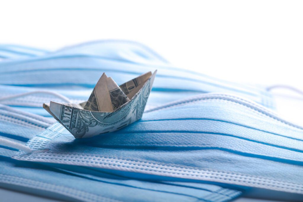 a dollar folded into an origami paper boat floating on a sea of masks