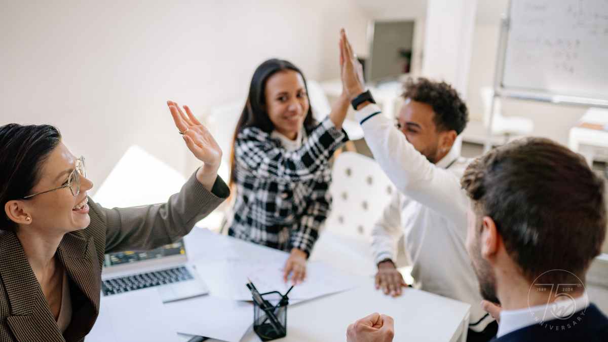Four diverse employees in bright office space high fiving and smiling