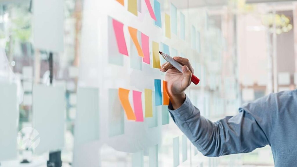 Person writing on a glass wall covered with colorful sticky notes, representing nonprofit planning and strategy development.