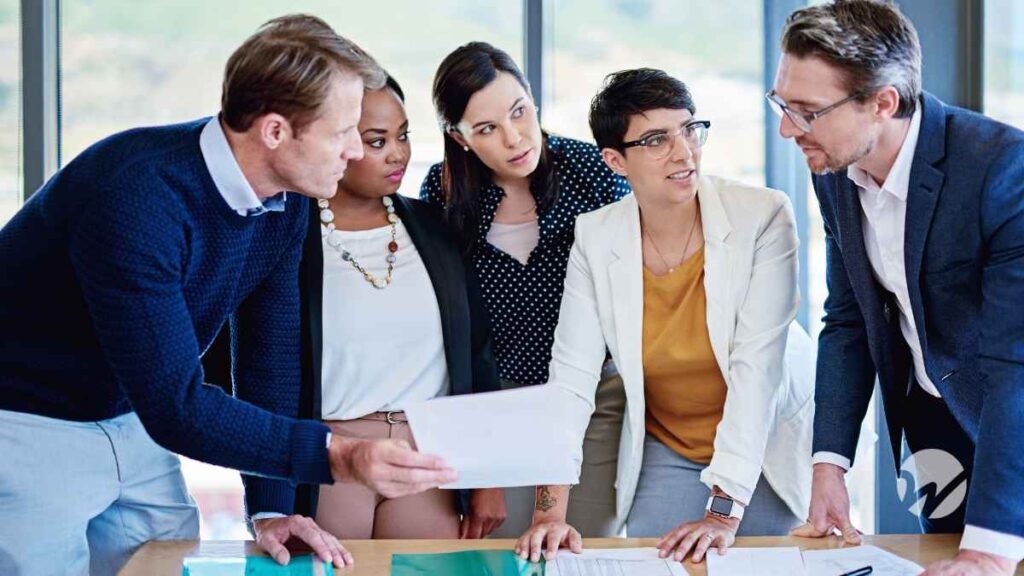 A diverse group of professionals gathered around a table reviewing financial documents during a meeting.