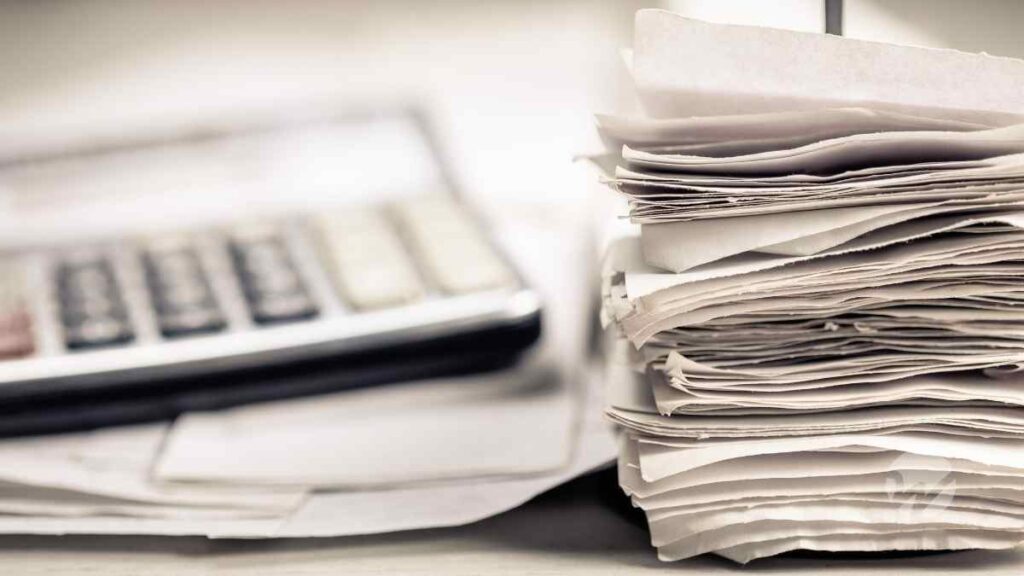 gray calculator placed next to large stack of business receipts representing business expenses