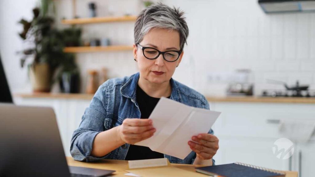 Woman in her 60s reading IRS notice at desk with laptop open.