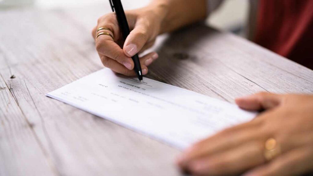 feminine hands signing a check on a wooden table meant to signify international charitable giving