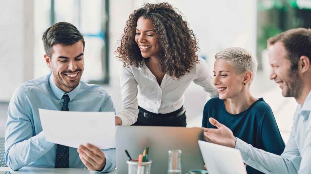Four professionals in a collaborative meeting, smiling as they review a document, representing an engaged and effective board.