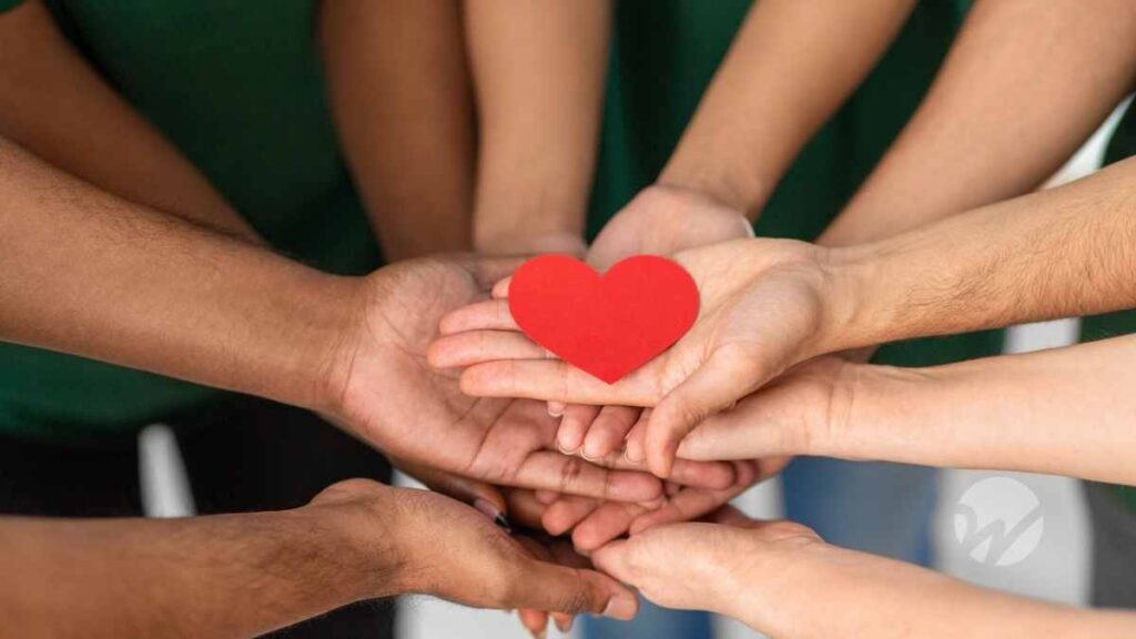 several hands stacked on one another palm up holding a paper heart illustrating nonprofit collaboration