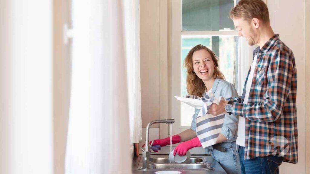 Young couple washing dishes together while laughing