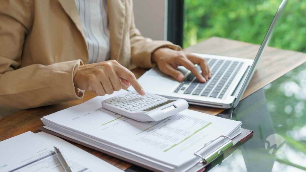 feminine figure working at desk typing on computer and using calculator