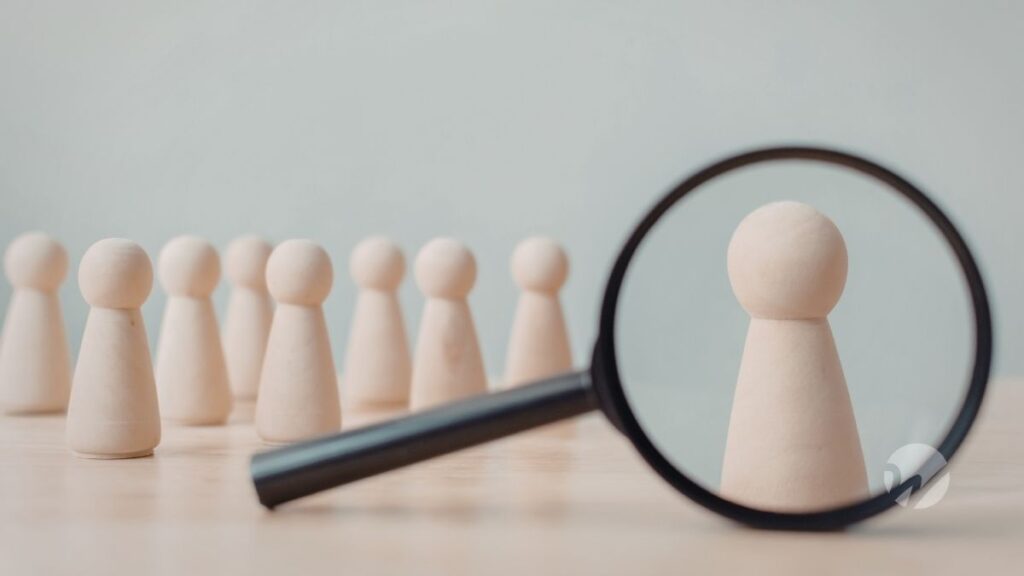 Wooden figures with one figure highlighted through a magnifying glass, representing the process of choosing a nonprofit audit firm.