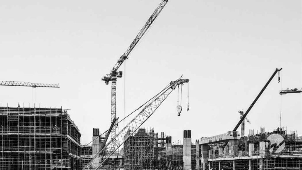 black and white photo of large scale construction site with three large cranes