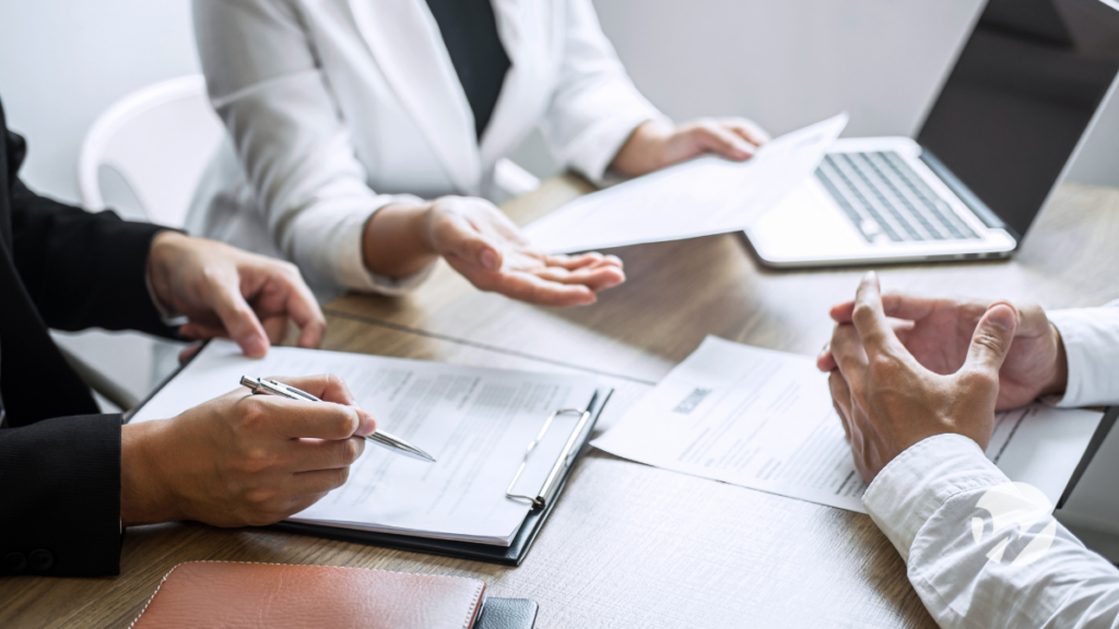 three professionals in business attire discussing paperwork at conference table