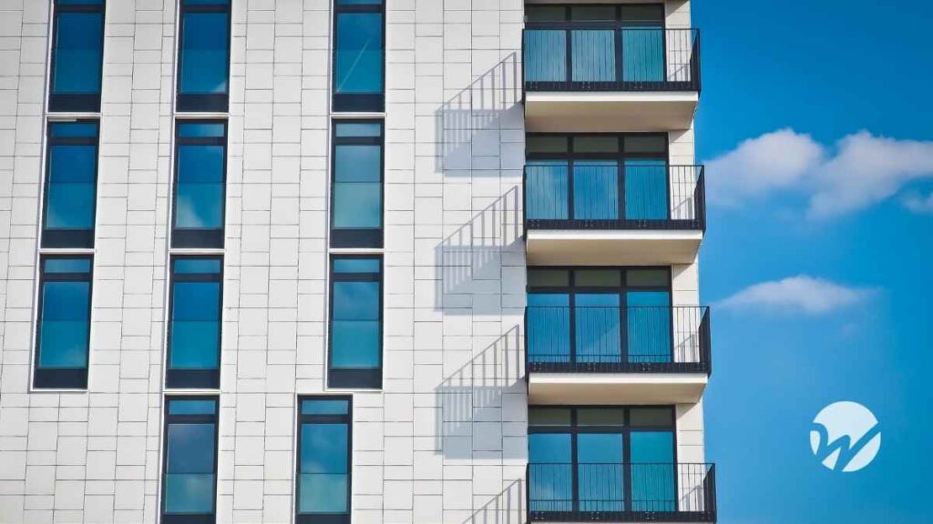 Photo of an apartment building with white facade against blue sky with clouds