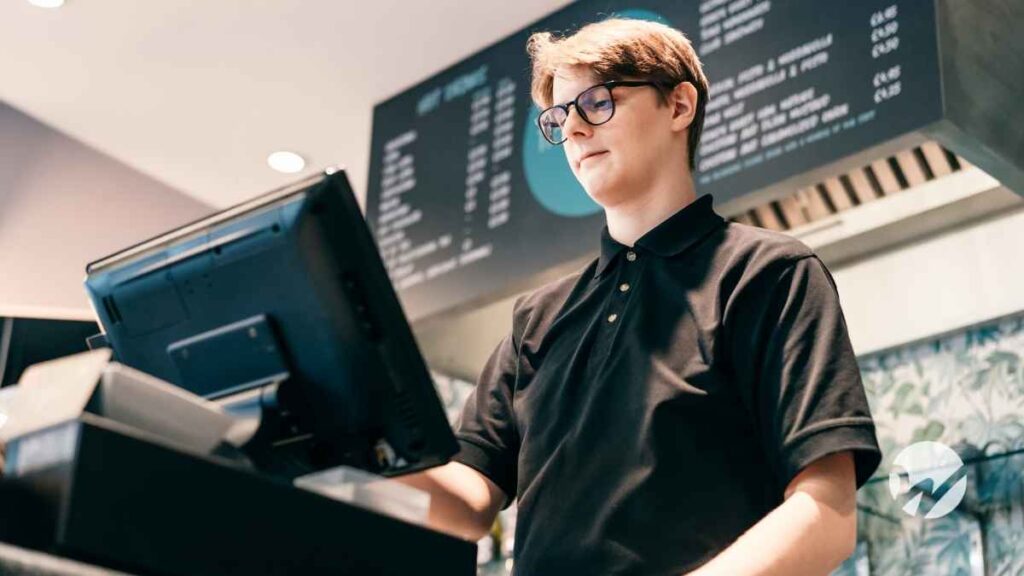 Caucasian teen male with brown hair behind a cash register at a cafe